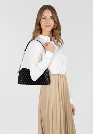 Borsa a mano nera trapuntata con un design strutturato, caratterizzata da una sottile tracolla e dettagli in catena. Indossata con una blusa bianca e una gonna beige.