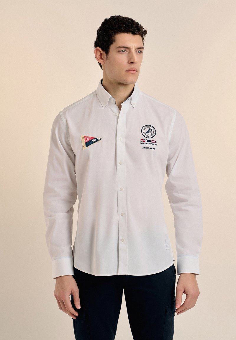 Camisa de botones blanca de manga larga con parches de logo; presenta un collar clásico, un dobladillo recto y una textura de tela suave de algodón.