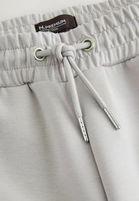 Light gray joggers with an elastic waistband, drawstring, metal eyelets, and smooth texture. Features a fabric label inscribed "N.PREMIUM."
