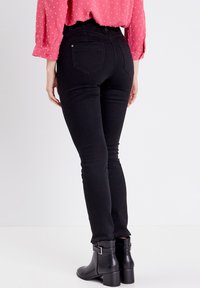 Jeans noirs taille haute avec une coupe skinny. Caractéristiques de deux poches arrière et d'une fermeture à bouton. Associés à des bottines noires.