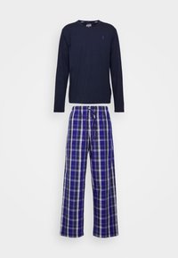 Marineblauwe top met lange mouwen en ronde hals boven een geruite pyjamabroek in blauw, wit en paars, met een tailleband met trekkoord en knoopsluiting.