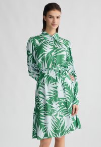 Vestito verde e azzurro chiaro con motivo a foglia di palma, maniche lunghe, chiusura a bottoni e una cintura abbinata in vita. Tessuto morbido.