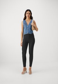 Denim ærmeløs top med V-hals og knapper foran, parret med sorte tætsiddende bukser og lyse strop sandaler. Neutral håndtaske.