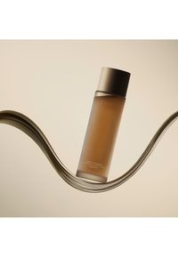 Bruine glazen fles met een metalen deksel, gelabeld "Huxley Secret of Sahara Conditioning Essence Toner." Gewone textuur, minimalistisch ontwerp.