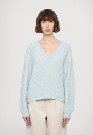 Suéter de punto azul claro con escote en V, hombros caídos y puños acanalados. La tela parece suave y texturada con un ajuste holgado.