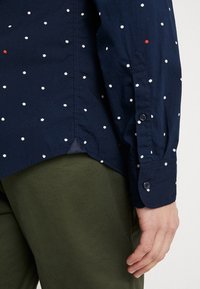 Marineblå skjorte med hvidt og rødt prikkemønster, manchet med knapper og sideslidse. Fremstillet af bomuld med en glat tekstur og skræddersyet pasform.