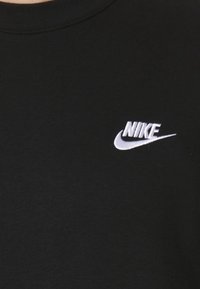 Svart t-shirt med rund hals, med en vit broderad Nike-logotyp på vänster bröst. Slät textur, avslappnad design.