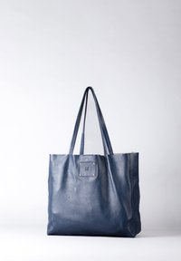 Navy leather tote bag with two long handles, a flat rectangular shape, textured surface, and a stitched square accent with metal studs.