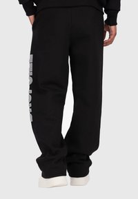 Schwarze Jogginghose mit lockerer Passform, mit einem weißen Grafikdesign am linken Bein und gerippten Bündchen. Hergestellt aus weichem Baumwollmaterial.