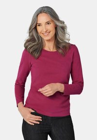 Langärmliges, rundhalsiges Shirt in Fuchsia, aus weicher Baumwolle, kombiniert mit dunklen Jeans. Die Textur wirkt glatt mit minimalen Details.