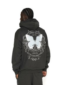 Schwarzer Kapuzenpullover mit großem weißen Schmetterlingsdruck auf dem Rücken, der kunstvolle grafische Elemente und Text enthält, aus einem weichen Stoff gefertigt.