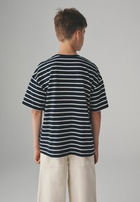 Camisa de rayas marinas con mangas anchas, con rayas blancas horizontales, corte casual, fabricada en tela suave, combinada con pantalones de pierna ancha color beige claro.