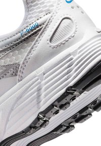 Gros plan sur le talon d'une chaussure de sport blanche avec une semelle texturée, un panneau en mesh, et le texte bleu "P-6000" près du col rembourré.