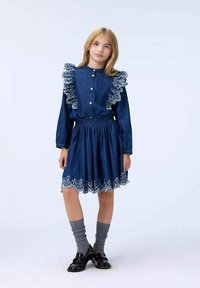 Denimová šaty s volánovým límcem a manžetami, modré barvy, s elastickým pasem, vícevrstvou sukní a bílou květinovou výšivkou na lemu.