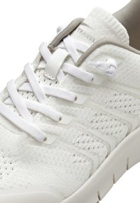 Scarpa da ginnastica bianca con tomaia in maglia testurizzata, lacci bianchi piatti e un accento grigio chiaro. Presenta una suola ammortizzata e sovrapposizioni laterali.