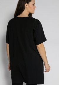 Black oversized t-shirt with short sleeves, made of soft cotton. Smooth texture, simple design, and a rounded neckline. No patterns or accents.