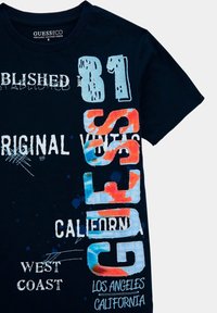 T-shirt in cotone blu navy con testo e grafiche colorate. Gli elementi chiave includono "81," "GUESS," e "CALIFORNIA." Design usurato e a strati.