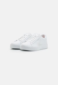 Białe sneakersy z gładką, syntetyczną cholewką, zaokrąglonym noskiem, płaskimi sznurowadłami oraz teksturowaną gumową podeszwą. Subtelne logo na boku.