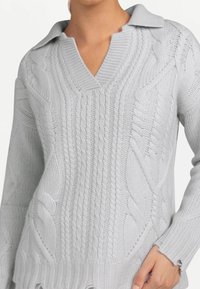 Ljusgrå stickad tröja med V-ringning och mjuk krage; har detaljerade kabelmönster och ribbade mudd för textur.