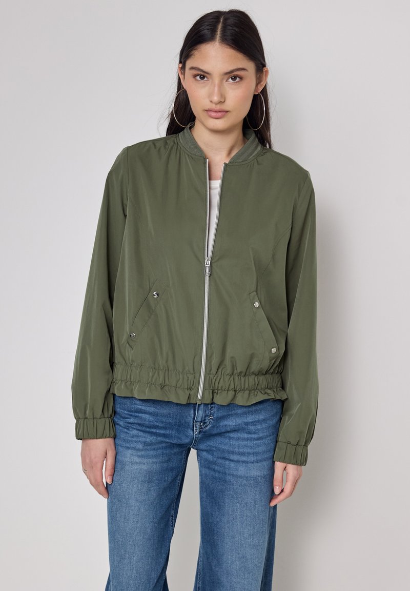 Giacca bomber verde oliva con zip, polsini elasticizzati e orlo con cordoncino. Presenta un tessuto liscio e due tasche laterali.