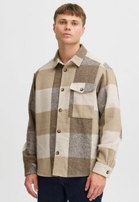 Camicia di flanella a quadri in tonalità beige e marrone, con taschino anteriore, chiusura con bottoni e colletto. Tessuto morbido con una vestibilità rilassata.