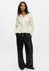 Haut peplum crème clair avec un décolleté en V et un détail à nouer, associé à un pantalon large noir pailleté et fluide, offrant un contraste de texture et de couleur.