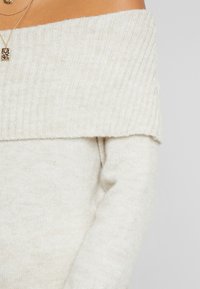 Helles beige, schulterfreies Sweatshirt aus weichem, geripptem Strickstoff; verfügt über lange Ärmel und einen weiten Ausschnitt für eine lockere Passform.