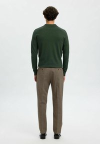 Grøn strikket polo med krave, parret med lysbrune mønstrede bukser, der har en slim fit og to-knaps lukning på ryggen.