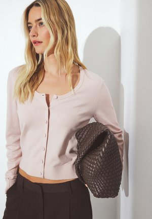 Lichtroze geribbelde cardigan met ronde halslijn en knoopsluiting, gecombineerd met een gestructureerde donkerbruine geweven handtas.