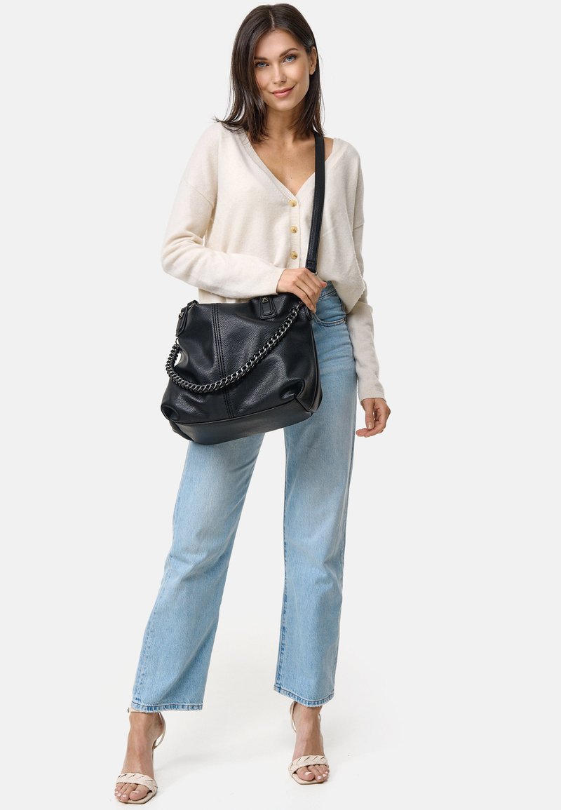 Zwarte leren handtas met een kettinghandvat, slappe ontwerp, gestructureerde afwerking, gecombineerd met lichtblauwe jeans en een crèmekleurige cardigan.