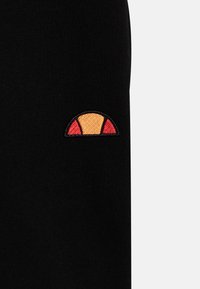 Schwarzer Stoff mit einem kleinen bestickten Design, das einen Halbkreis in Orange und Rot zeigt. Die Textur wirkt glatt und weich.