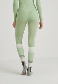 Light green leggings with a fitted design and textured panels. Accented with white, gray, and black striped patterns at the calves.