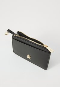 Zwarte leren portemonnee met gouden rits en hardware, voorzien van een logo-accent aan de voorkant en een slank, rechthoekig ontwerp.