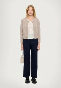 Vaaleanbeige neulecardigani napilla, valkoinen paita, tummansiniset leveät housut, mustat massiivipohjaiset kengät ja pieni vaalean laukku.