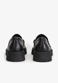 Czarne skórzane mokasyny z masywną czarną gumową podeszwą. Posiadają złote akcenty i gładką fakturę, zaprojektowane w zaokrąglonym kształcie.