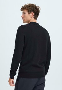 Pulover negru cu mâneci lungi, guler rotund, tiv și manșete ribbate, textură netedă și design ajustat. Stil minimalist, fără logo-uri vizibile.