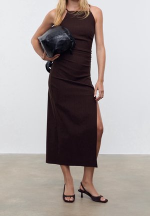Robe maxi côtelée marron avec un col haut et une fente latérale, accompagnée d'un sac en cuir noir et de sandales à talons foncés. Texture lisse.