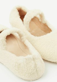 Cremefarbene Hausschuhe aus weichem, strukturiertem Stoff mit einer plüschigen Oberfläche und rundem Einstieg, die eine einfache, abgerundete Form haben.