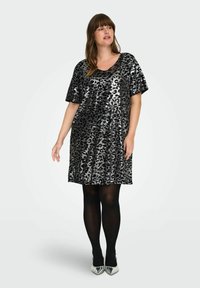 Juoda ir sidabrinė leopardų rašto blizgučių suknelė su trumpomis rankovėmis ir V formos iškirpte, pasižyminti laisvu siluetu, derinama su juodomis kojinėmis ir sidabriniais aukštakulniais.