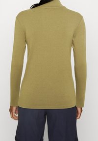 Maglia a maniche lunghe a coste in tessuto verde oliva, design aderente con colletto alto, abbinata a pantaloncini color navy.