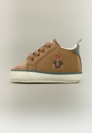Brun småbørnssneaker med ruskindtekstur, beige sål, snørebånd og en bamse med en rød hat broderet på siden.
