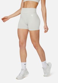 Shorts deportivos grises de cintura alta con una textura suave, con un logo blanco en el muslo izquierdo. Combinados con zapatillas y calcetines blancos.