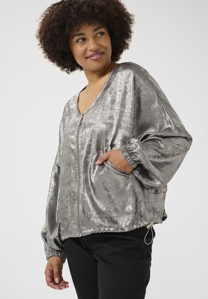 Silberne metallische Jacke mit V-Ausschnitt, Reißverschluss, elastischen Manschetten und zwei Seitentaschen; glatte Textur mit glänzendem Finish.