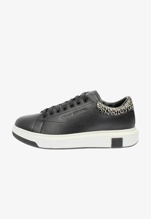 Baskets en cuir noir avec semelle en caoutchouc blanche, bout rond et lacets noirs. Détail de logo notable en blanc sur le talon. Texture lisse.