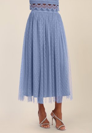 Light blue midi skirt with sheer polka-dot overlay paired with silver high-heeled sandals on tan legs against a beige background.