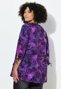 Paarse tuniek met een doodshoofd- en rozenpatroon, met 3/4 mouwen met strikjes en een losse pasvorm. Gladde stofstructuur, levendige kleurcontrast.