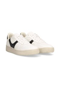Zapatillas de cuero blancas con un acento negro, diseño perforado en la puntera, suela de goma plana beige y cierre tradicional de cordones.