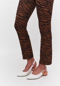 Valkoiset slingback-kengät, joissa on terävä kärki ja vaaleanruskea paksukanta, yhdistelevät ruskeisiin housuihin, joissa on musta tiikeriraidallinen kuvio.