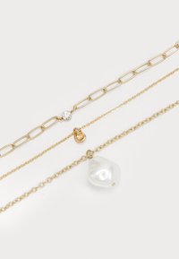 Tričko zlatých retiazok na bielom pozadí, jedna s čistým kamienkom, jedna s malým zlatým príveskom a jedna s veľkým bielym perlou ako príveskom.