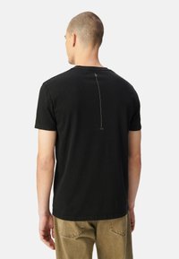 Camiseta de algodón negra con cuello redondo y mangas cortas, con un detalle de costura vertical en la parte posterior y un ajuste relajado.